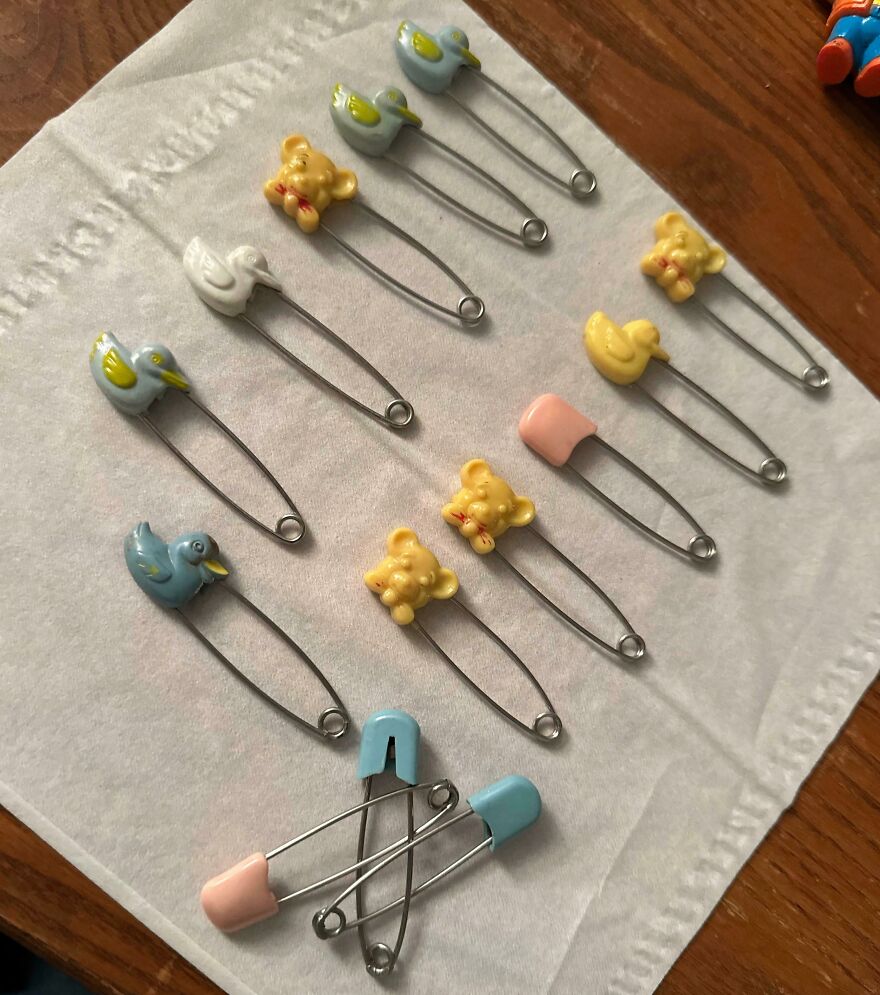 Assorted baby safety pins with animal designs, like a Gold Bar, found in Goodwill bins, on a white tissue.