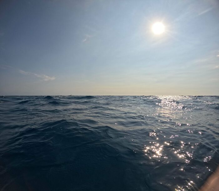 Sunlight glinting off vast, uncomfortable water, making you feel small. An open ocean view with bright sun in the sky.