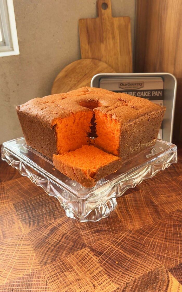 Square shaped orange cake with a slice cut out displayed on a glass stand