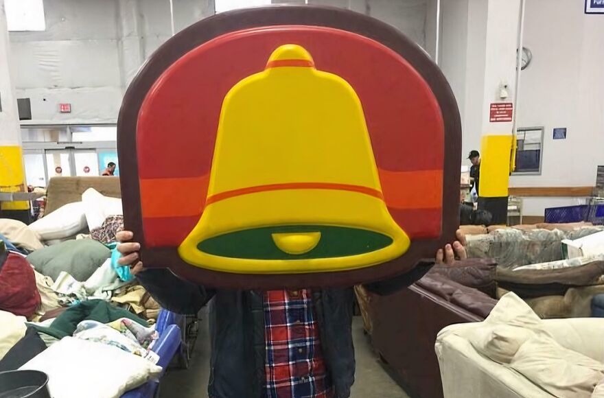 A person holding a large Taco Bell sign found in the Goodwill bins. This Gold Bar-like find is surprisingly good.