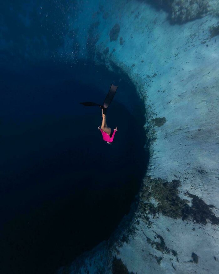 A lone swimmer in a pink top and black fins descends into dark, uncomfortable water, making them feel small.