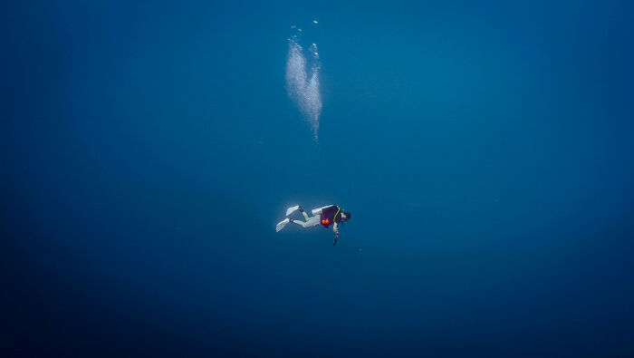 A lone diver suspended in deep, dark blue water, with bubbles rising. This uncomfortable water pic makes you feel small.