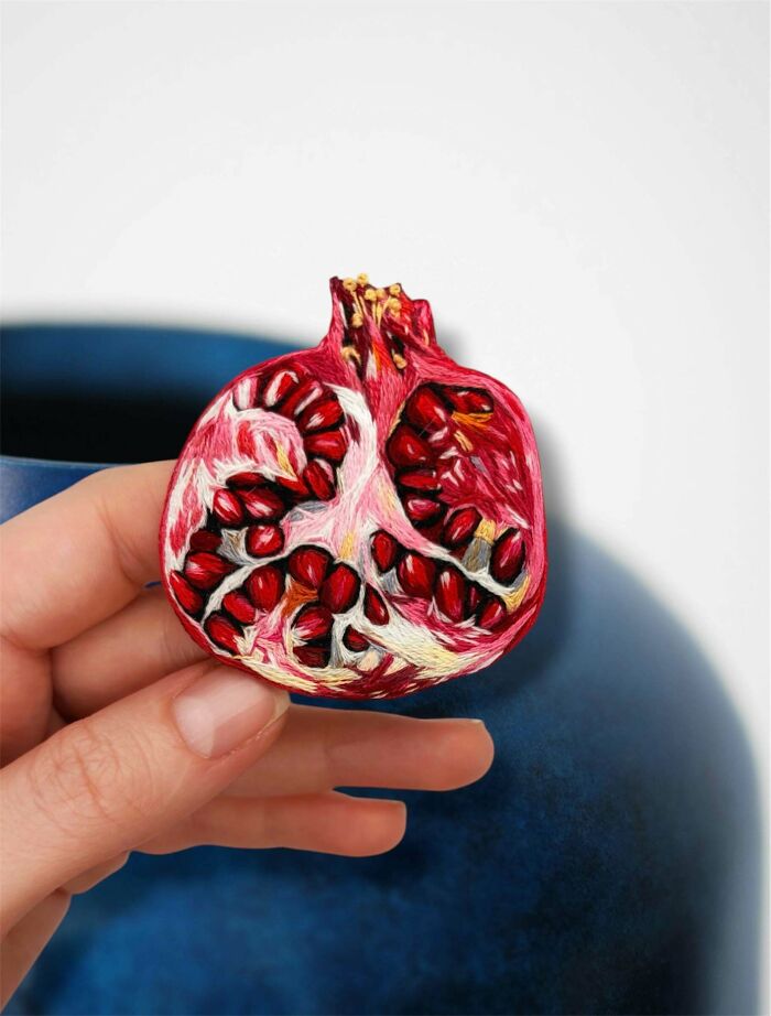 An embroidered pomegranate slice held between fingers, a detailed handmade project.