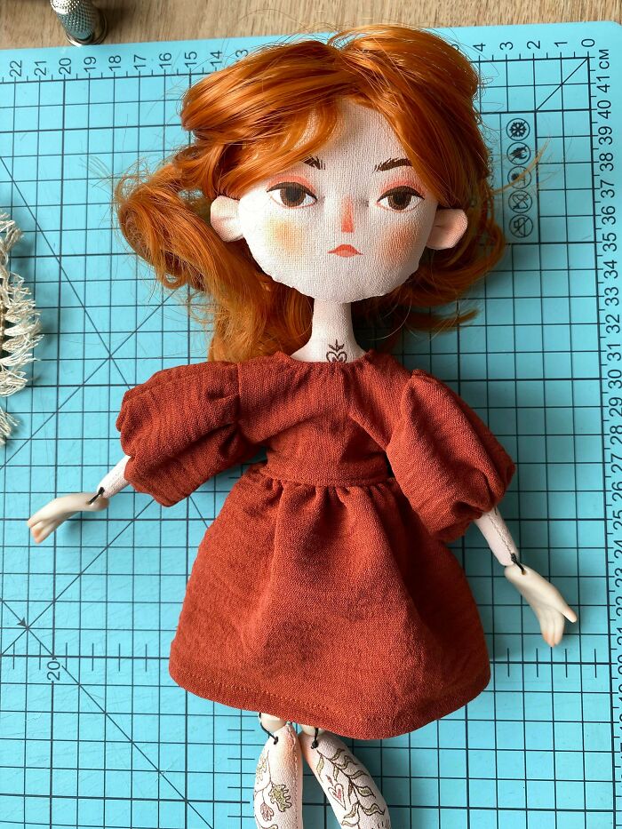A handmade fabric doll with red hair and a terracotta dress, displaying creative talent.