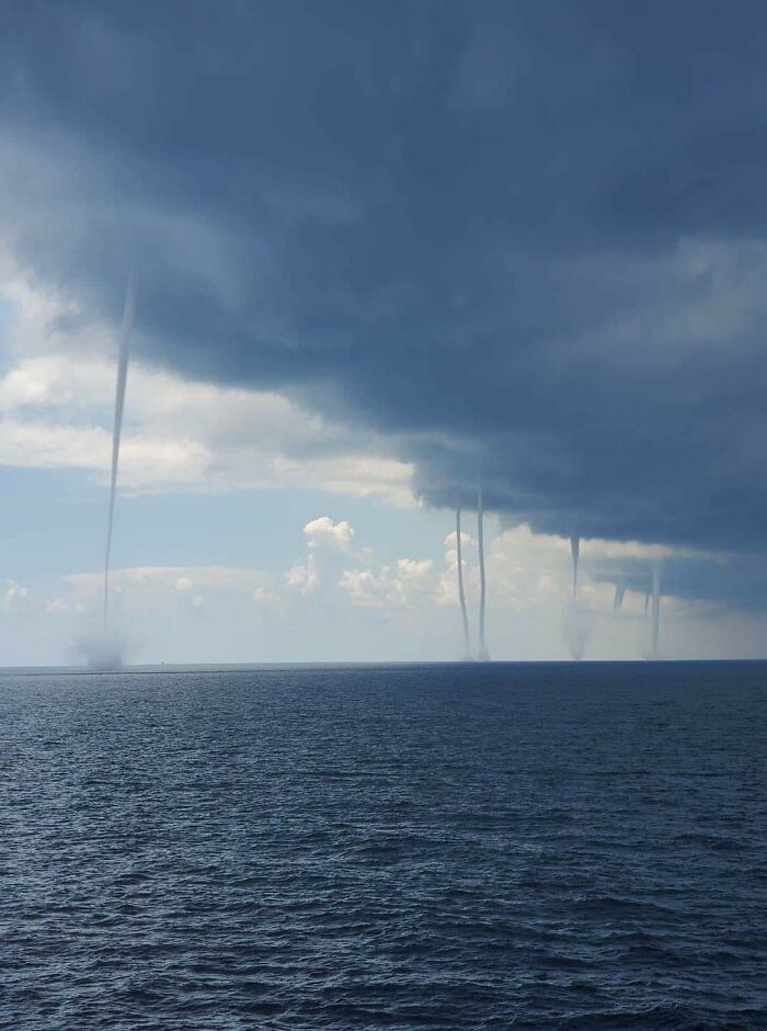 Multiple towering waterspouts stretch from dark clouds to the vast, uncomfortable water surface. They make you feel small.