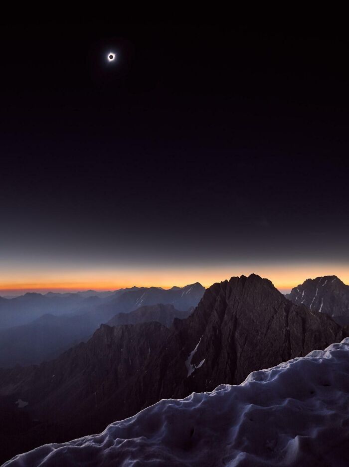 Unbelievable photos of a solar eclipse over snow-capped mountains at sunset, feeling like glimpses into another universe.