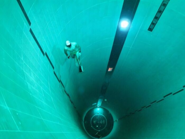 A lone diver appears tiny in a vast, deep pool, creating an uncomfortable water pic that makes you feel small.