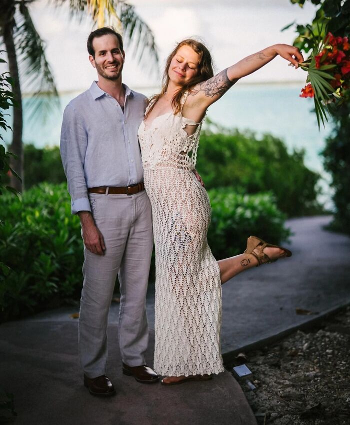 A happy couple posing in a tropical setting. The woman is wearing a beautiful crocheted dress, showcasing awesome crochet work.
