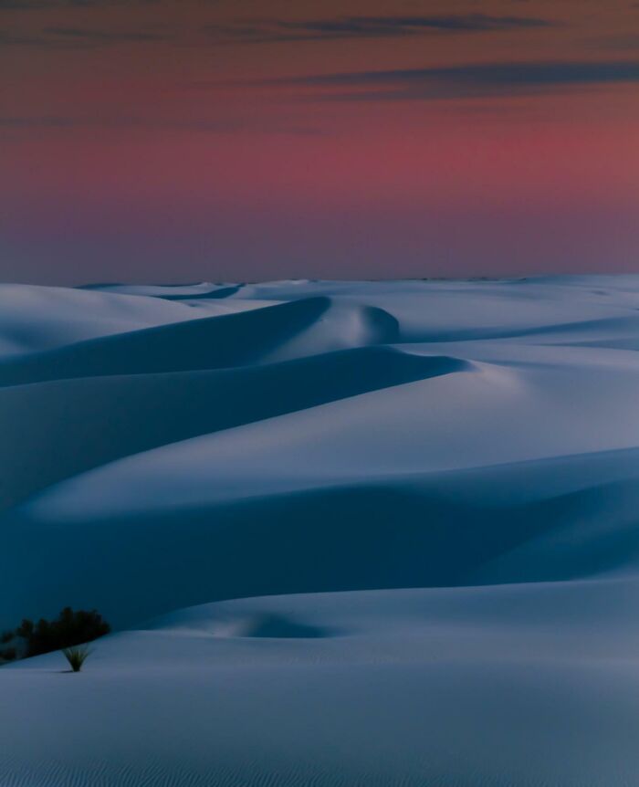 Unbelievable photos taken on Earth: Serene white dunes under a vibrant pink and purple twilight sky, feeling like another universe.