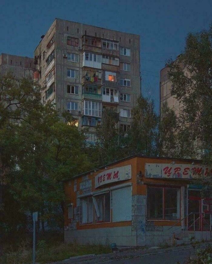 Dimly lit urban residential buildings with closed shop under evening sky