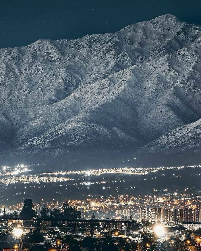 Uplifting posts: A breathtaking view of a city illuminated at night, nestled below majestic snowy mountains.