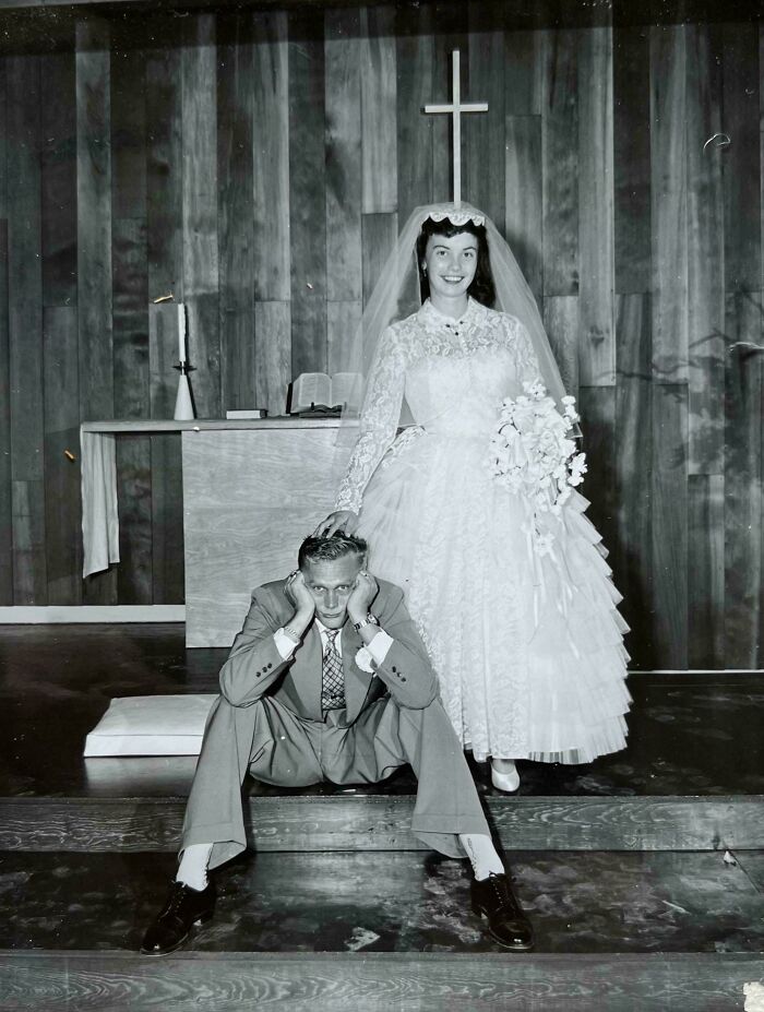 Candid old photo of a newlywed couple in a church, the groom playfully poses in front of his bride.