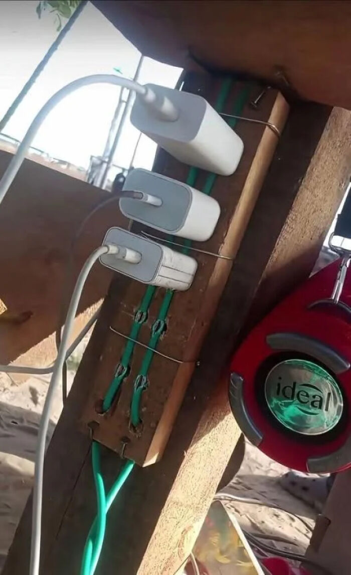 A perilous DiWHY charging station with three adapters wired to a wooden plank, exemplifying a failed DIY attempt.