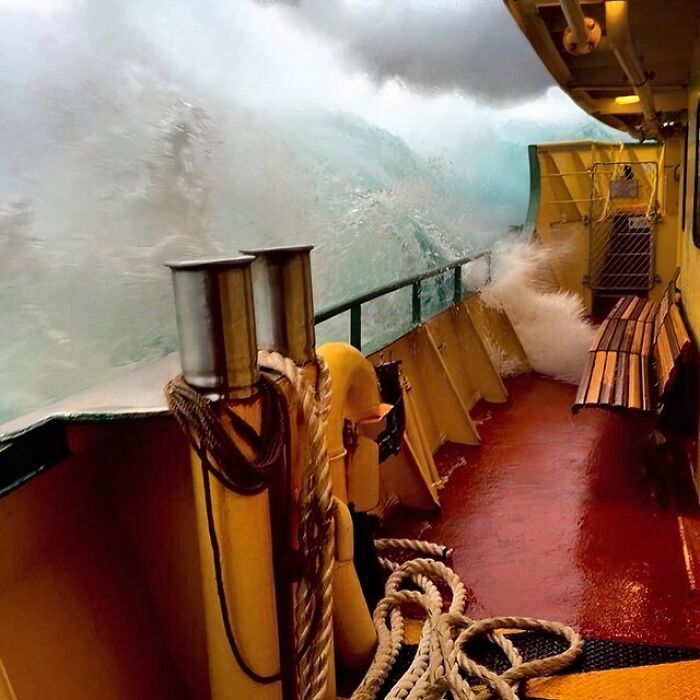 A massive wave crashes over the side of a boat, creating an uncomfortable water pic. The deck is red and yellow with ropes.