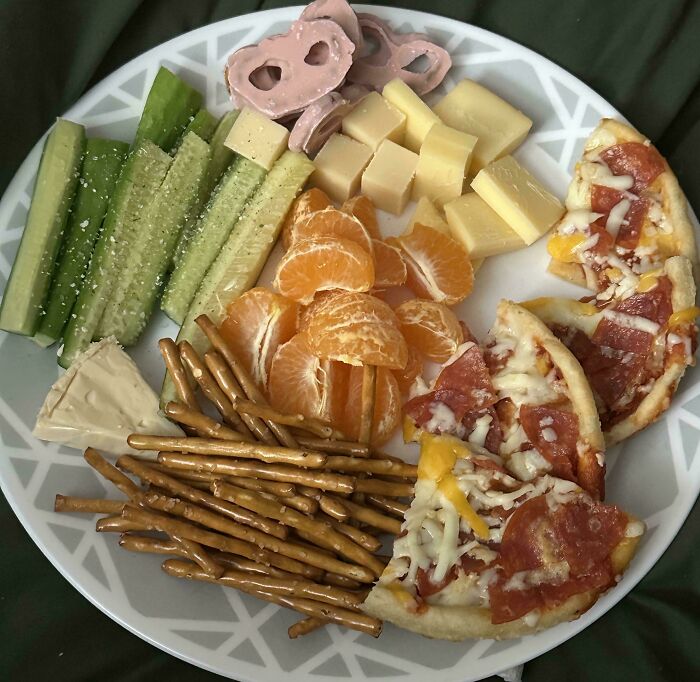 A delicious girl dinner plate with mini pizzas, cheese cubes, celery, tangerines, pretzels, and chocolate-covered pretzels.