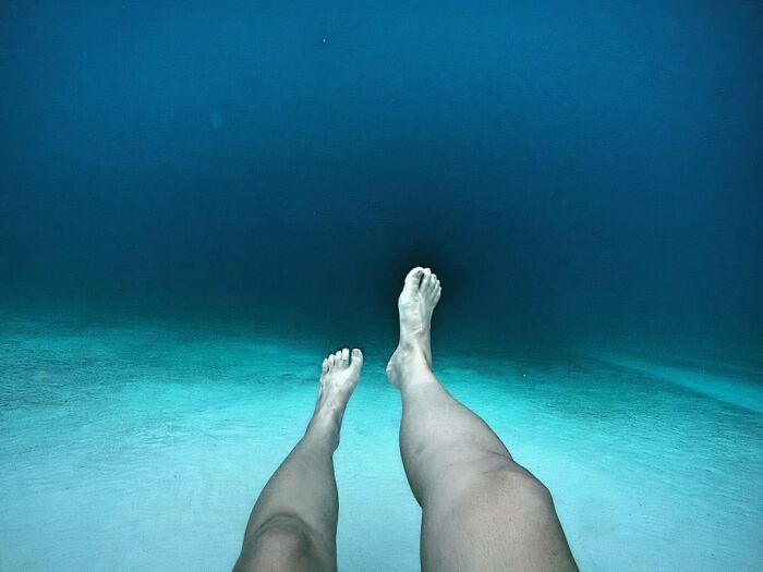 Legs dangle over deep, clear ocean water, showcasing uncomfortable water pics and the immense depth below.
