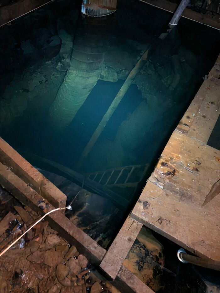 Uncomfortable water pics of a dark, murky flooded mine shaft with submerged ladder, pipe, and wooden beams.