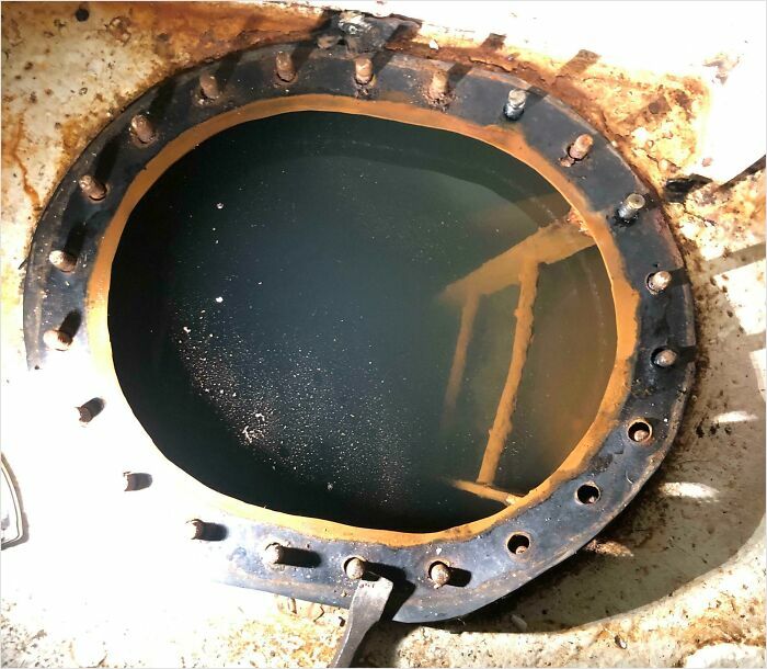 Uncomfortable water pic of murky water in a rusted metal access hatch, a ladder descending into the gloom.