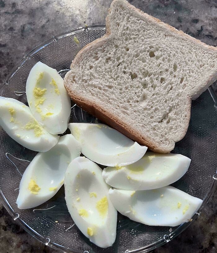 A simple girl dinner: sliced hard-boiled eggs and a slice of white bread on a clear glass plate.