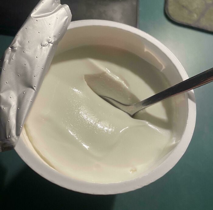 A partially opened yogurt container with a spoon, suggesting a simple Girl Dinner.