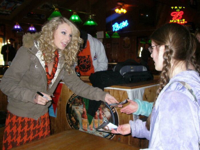 Wild photo of a celebrity encounter: Taylor Swift signing autographs for fans at a bar, looking friendly and engaged.