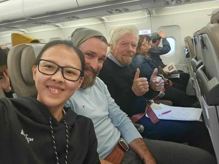 A woman takes a selfie on a plane with two men, including Richard Branson, offering thumbs up. Celebrity encounters beyond 'they were nice'.