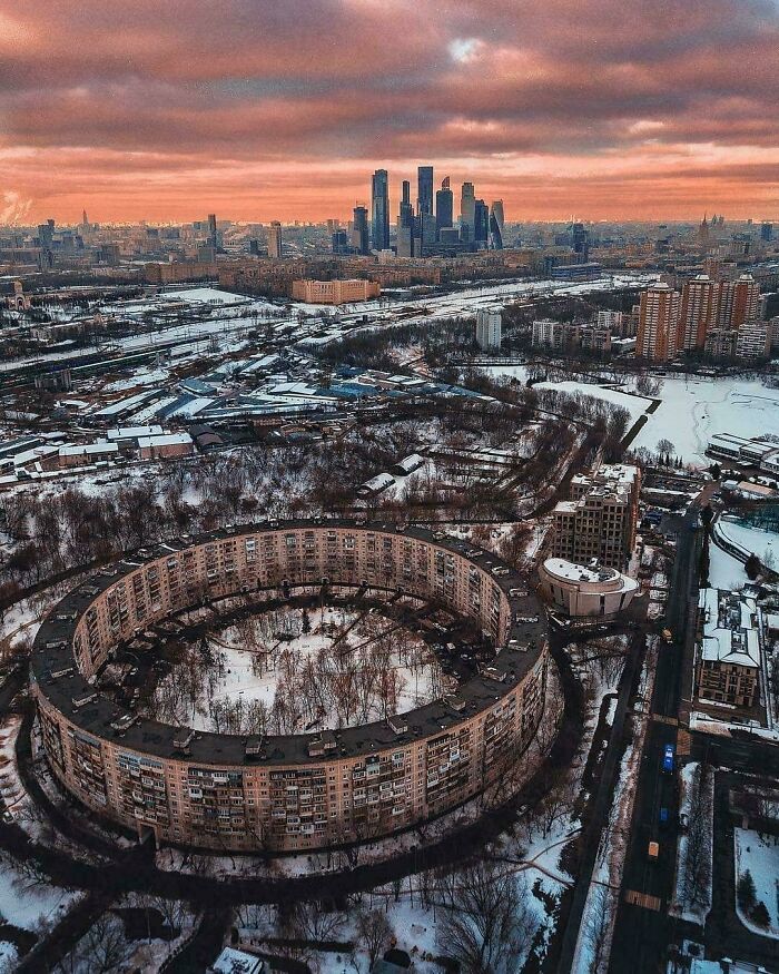 Snowy urban cityscape featuring circular residential building with skyscrapers at sunset