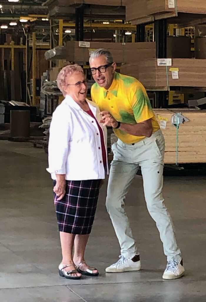 Jeff Goldblum wearing a yellow and green tie-dye shirt, glasses, interacting playfully with an older woman, a celebrity encounter.