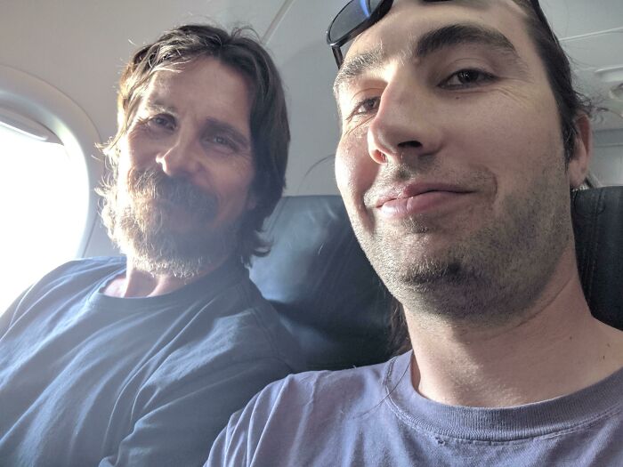 A man takes a selfie with actor Christian Bale on an airplane, capturing a wild celebrity encounter.