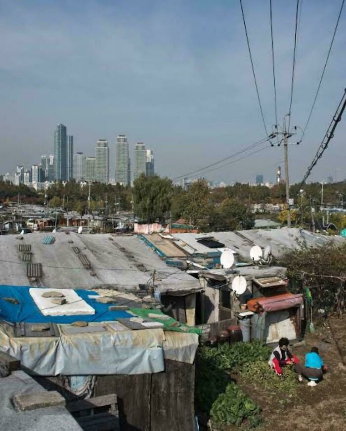 Shanty urban housing with satellite dishes and skyscrapers in the distant background