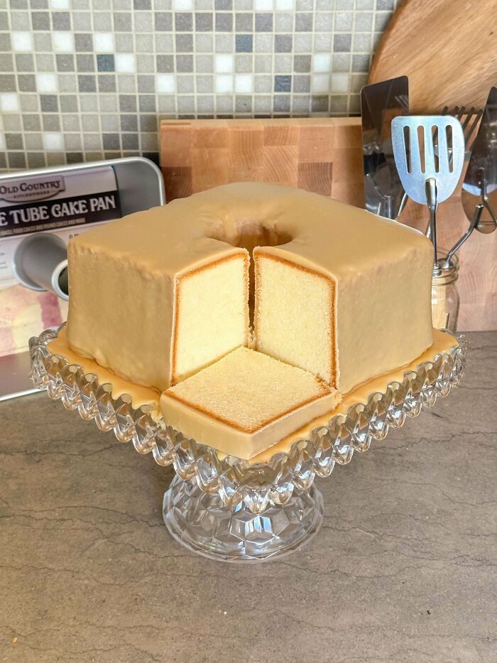 A square handmade cake with caramel glaze on a glass stand, showing baking talent.