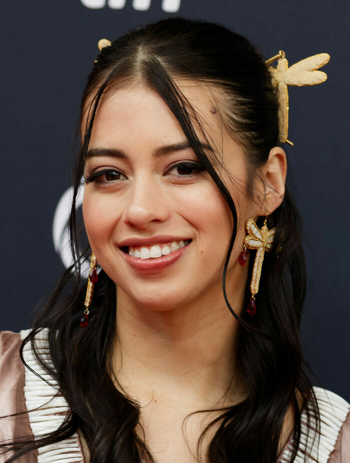 Amber Midthunder smiling, wearing ornate earrings and a dragonfly hair accessory, showcasing her career highlights.