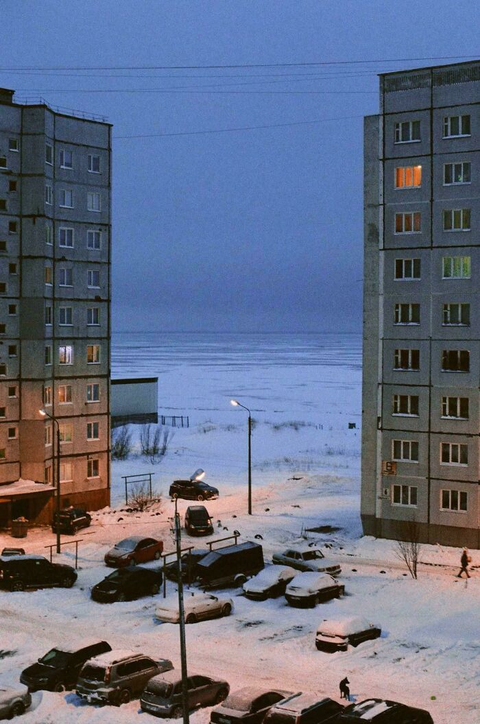 Snow-covered urban residential area with apartment buildings and parked cars at dusk