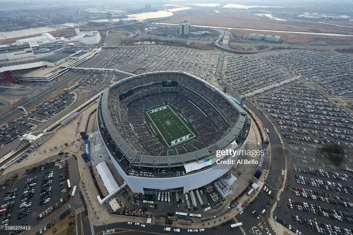 Aerial view of urban stadium surrounded by large parking lots and roads under cloudy sky