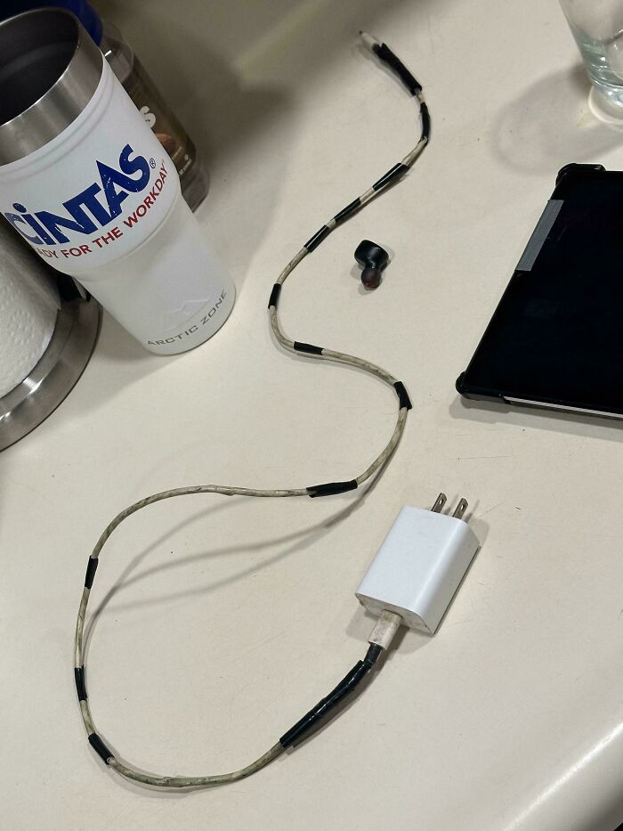 A makeshift phone charger and a GINTAS cup on a table, illustrating the reality of consumerism and price differences.