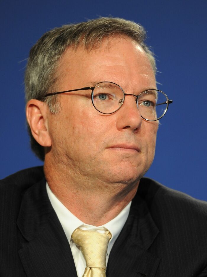 Eric Schmidt wearing glasses and a suit, with a blue background, portraying his career highlights.