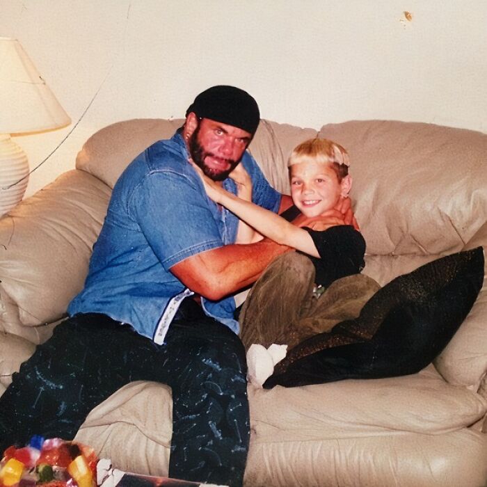 A bearded man in a black skullcap and a denim shirt with a smiling boy, sharing a wild celebrity encounter on a couch.