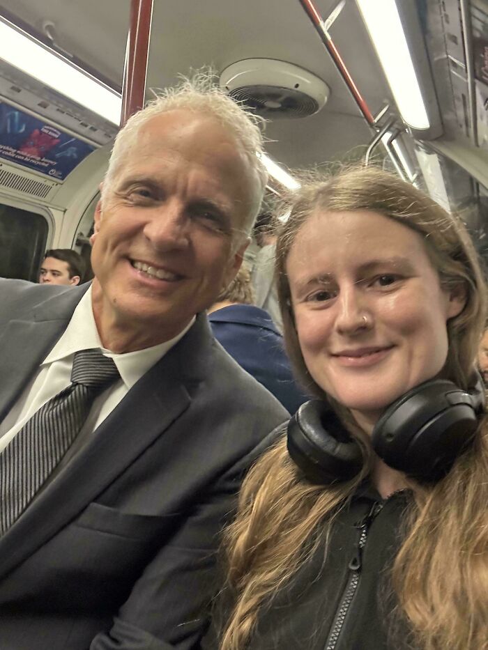 Smiling man in a suit and a woman with headphones on a train. A candid photo of a celebrity encounter.