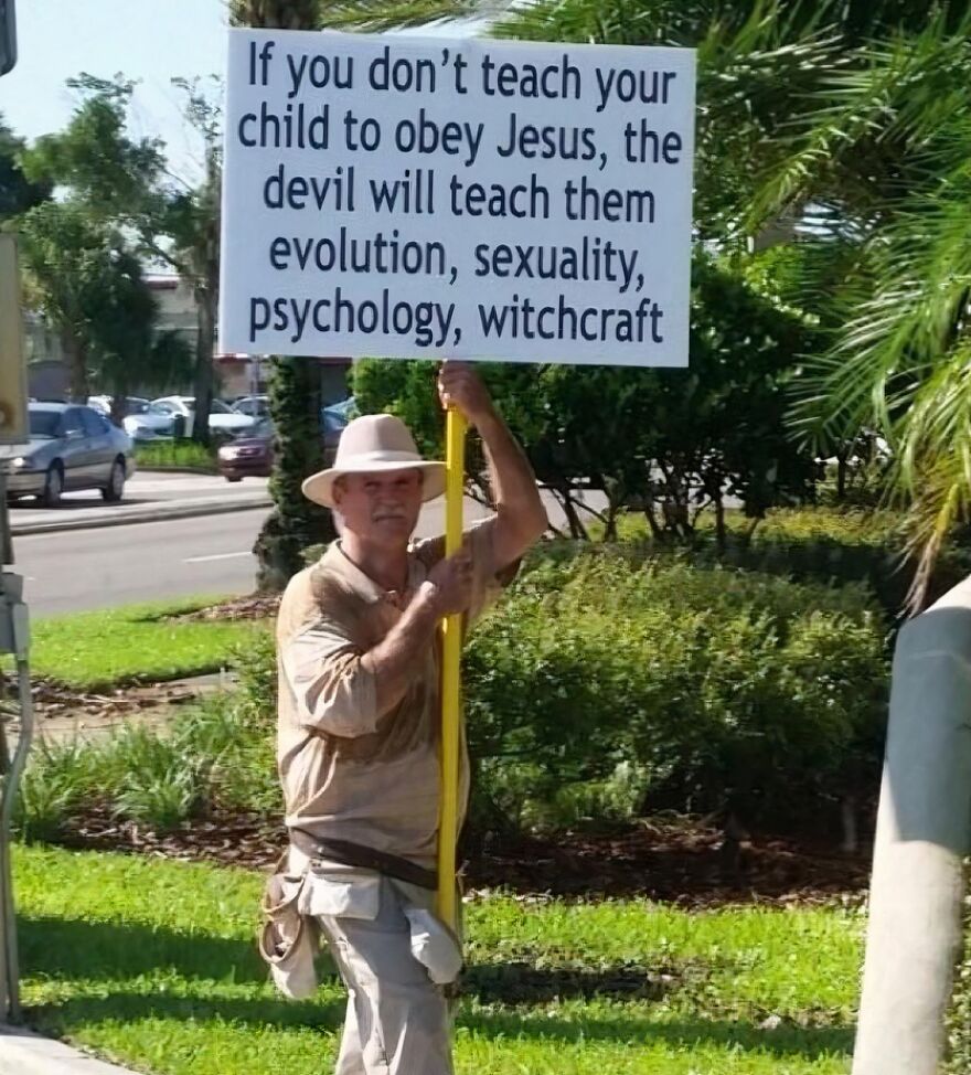 Man in a hat holding a sign about evolution, sexuality, and witchcraft, showing accidental LGBTQ+ allyship.