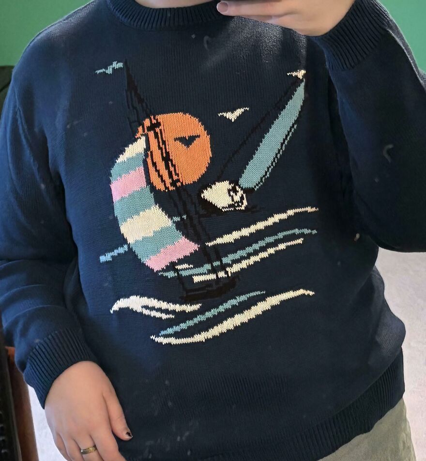 A person wearing a dark blue sweater with a colorful sailboat design, symbolizing LGBTQ+ allyship.