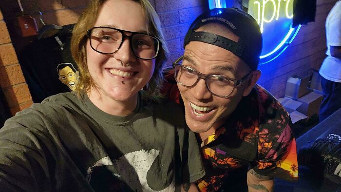 Two people smiling for a selfie, one in a graphic tee with a cartoon face, the other in a Hawaiian shirt. A unique celebrity encounter.