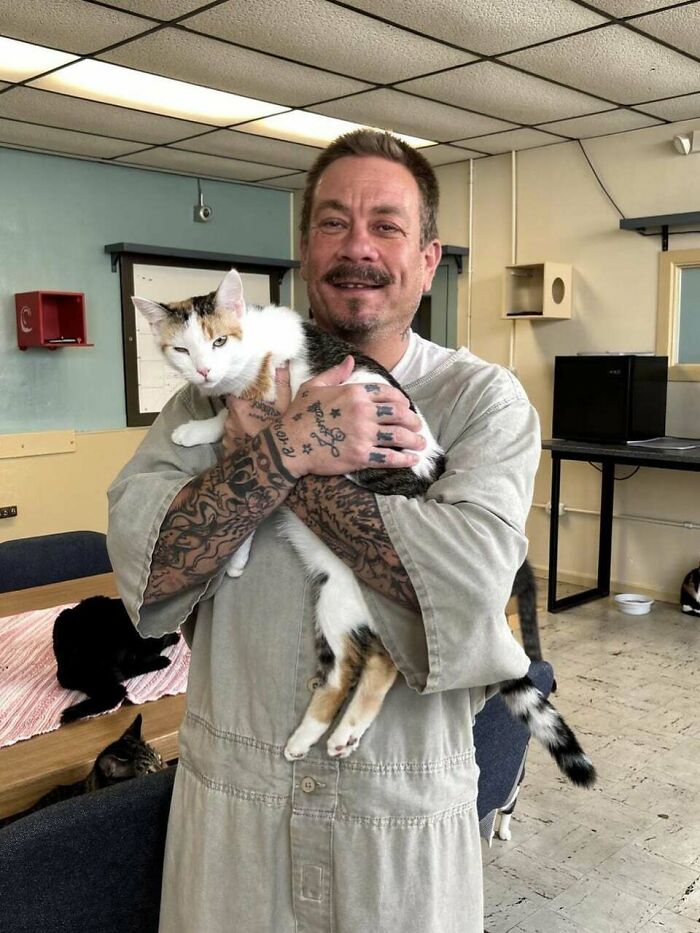 Uplifting post showing a man in a prison uniform holding a calico cat.
