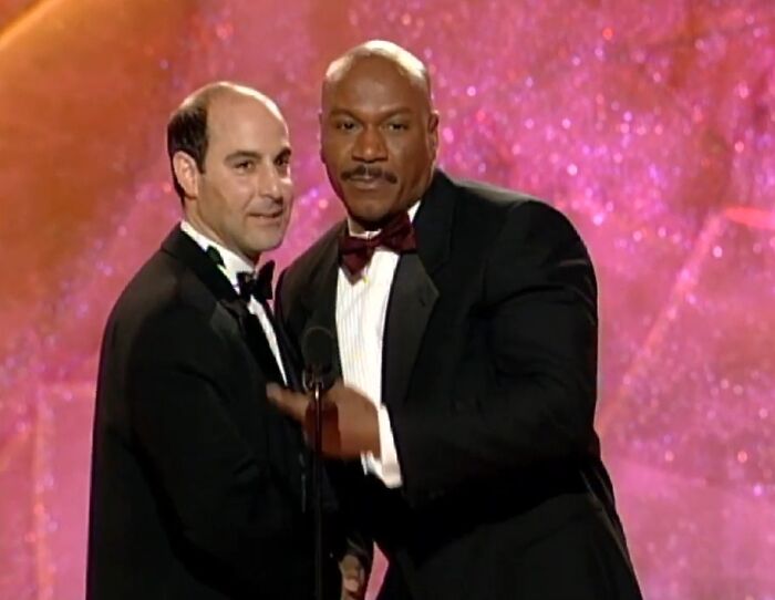 Two men on stage in tuxedos at an event illustrating celebrity friendships