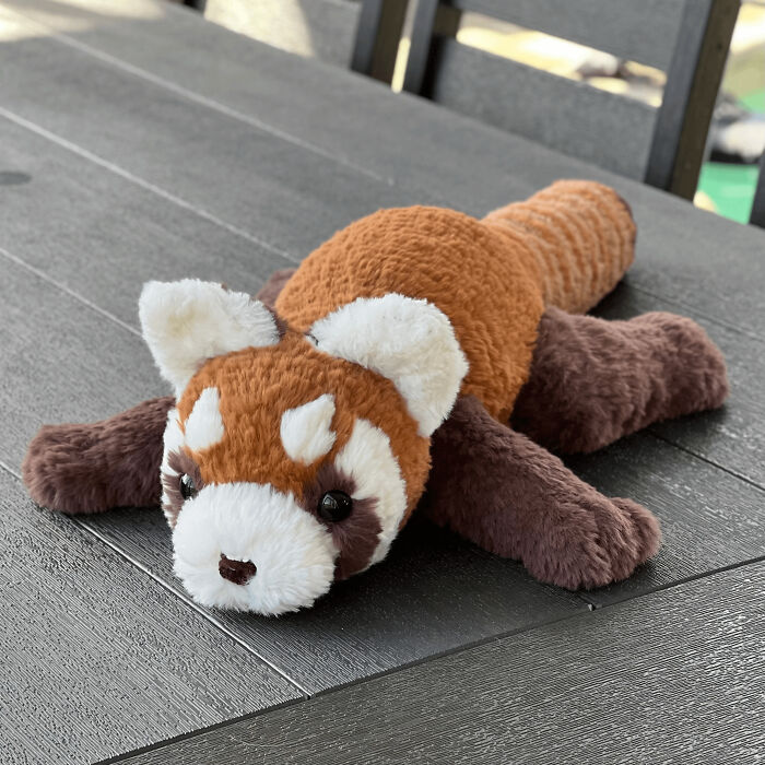 Soft, plush handmade red panda toy lying on a dark wooden surface, a cute handmade project with talent.