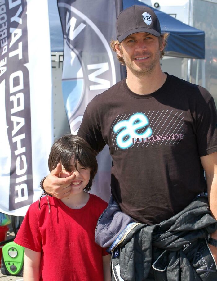 Paul Walker, in a black cap and AE Performance shirt, smiling with a child. A classic celebrity encounter photo.