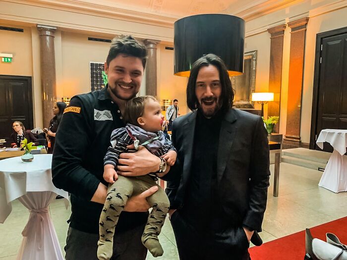 Wild photos of celebrity encounters: Keanu Reeves grinning with a man holding a baby at an event.