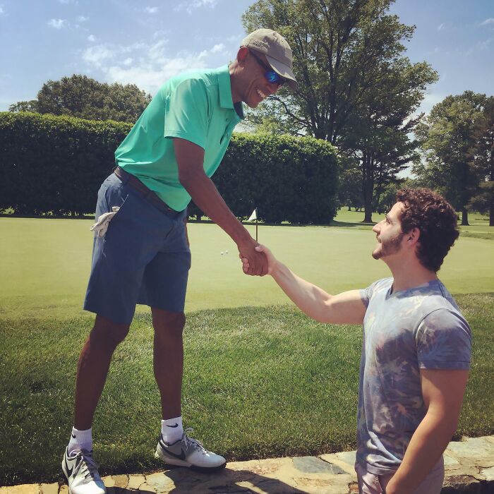 Barack Obama, wearing golf attire, smiles while shaking hands with a fan on a golf course. A wild celebrity encounter.