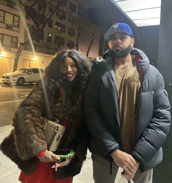 Celebrity encounters: SZA in a fur coat smiles next to a man in a blue Mets hat, outside at night.