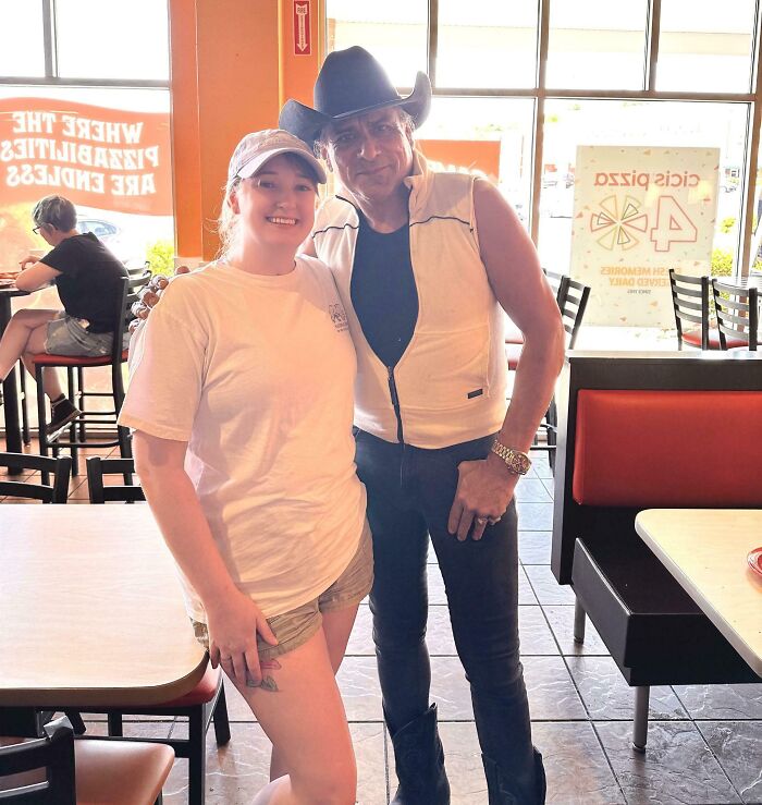 A woman in a cap and t-shirt smiling next to a man in a cowboy hat and sleeveless vest. A wild celebrity encounter.