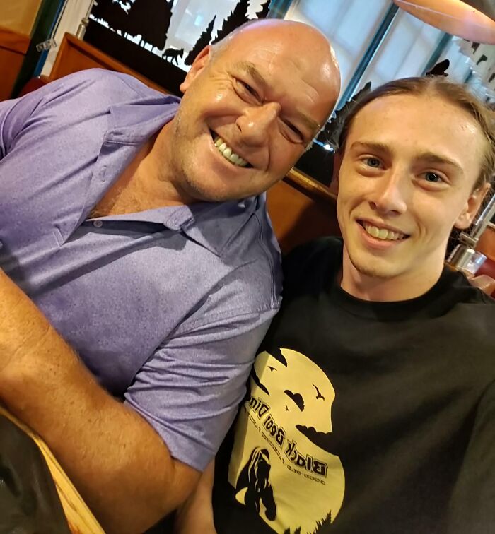 Bald man in purple shirt smiles with a younger man. A warm, friendly celebrity encounter.